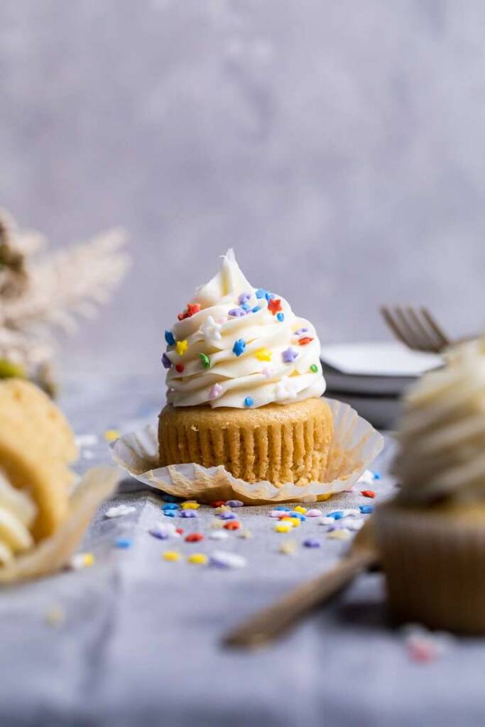 A single frosted vegan vanilla cupcake with rainbow sprinkles on top. 