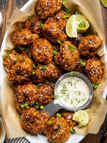 A white dish with brown parchment paper of baked vegan teriyaki cauliflower wings.