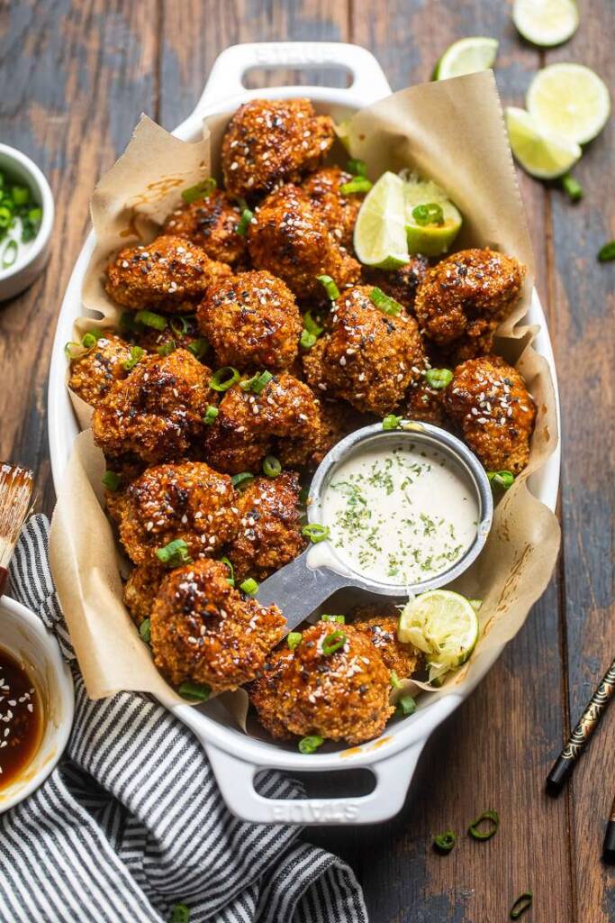 baked vegan teriyaki cauliflower wings with lime wedges and ranch dressing. 