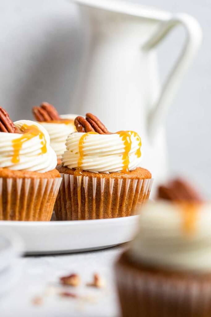 Three vegan carrot cake cupcakes with vegan cream cheese frosting and caramel drizzle.