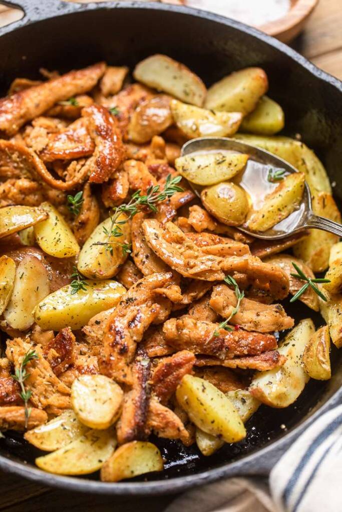 A close up of a skillet of vegan garlic butter chicken with chopped baby potatoes.