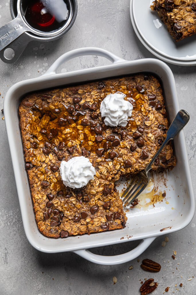 cooked vegan banana bread baked oatmeal with dairy free whipped cream in white casserole dish. 