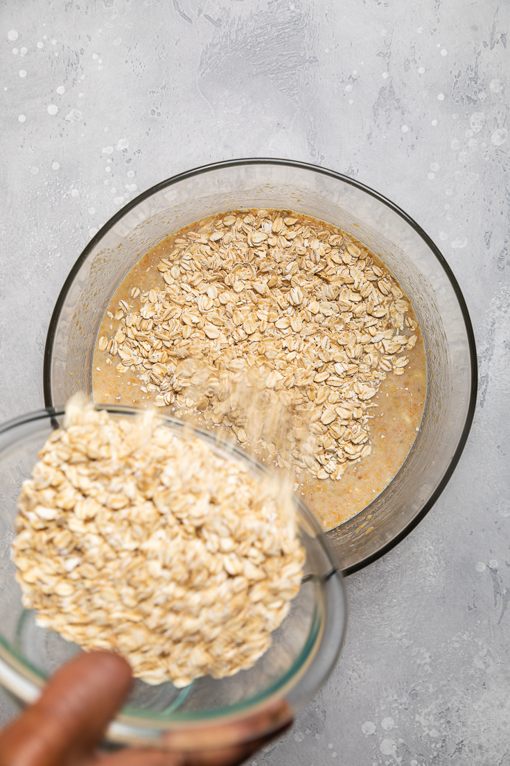 Pouring oats into a bowl with wet ingredients.