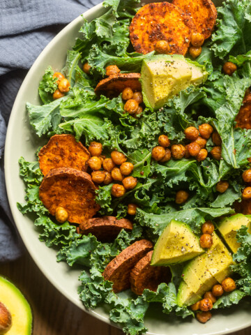 A plate of high protein vegan kale salad with chickpeas and cooked sliced sweet potatoes.