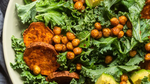 A plate of high protein vegan kale salad with chickpeas and cooked sliced sweet potatoes.