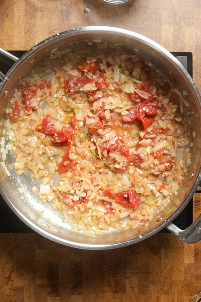 A pot of onions, thyme, garlic, ginger and tomatoes cooking. 