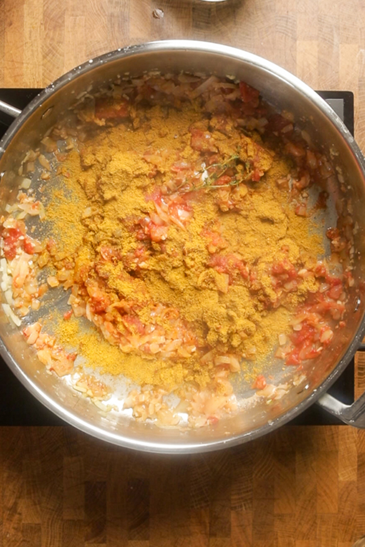 A pot of vegan curry ingredients mixed with tomato paste and spices.