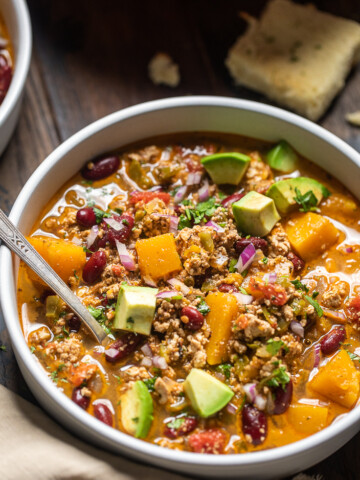 A bowl of vegan butternut squash chili with avocado cubes on top.