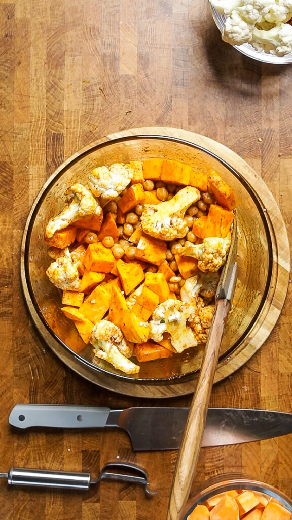 cauliflower and sweet potatoes in a bowl seasoned and stirred together. 