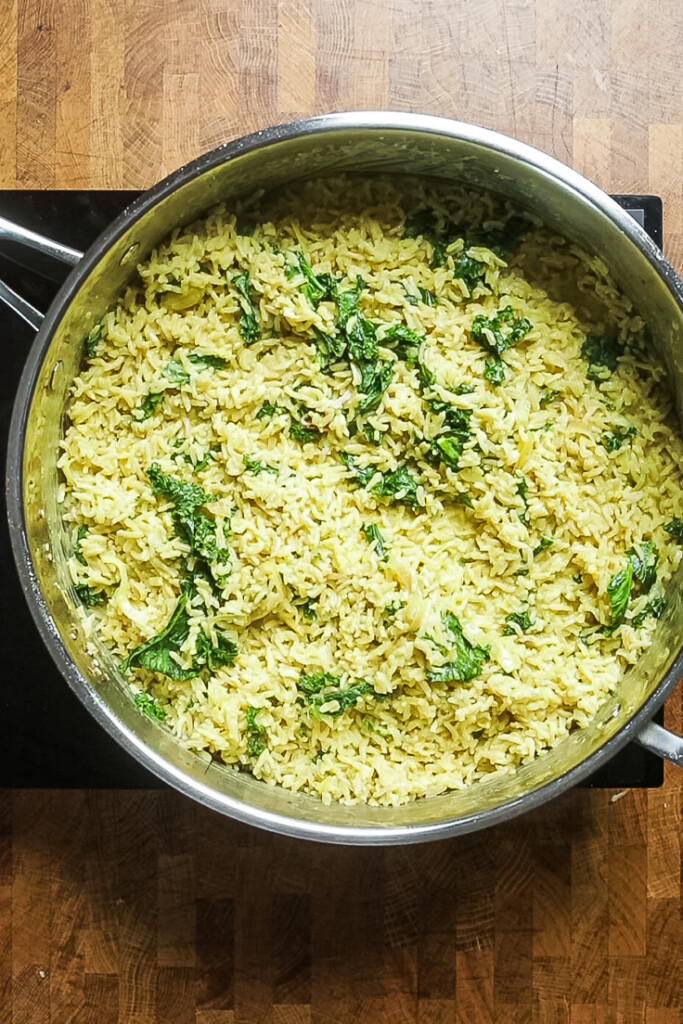 creamy coconut rice and kale cooking in a stainless steel skillet. 