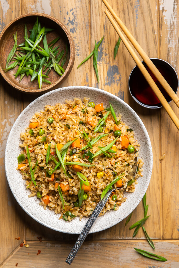 A bowl of vegan fried rice with vegetables with a bowl of soy sauce and chopsticks.
