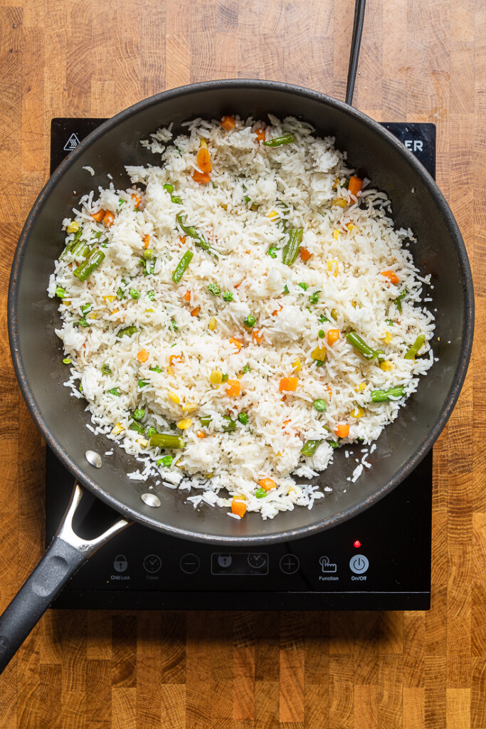 A skillet of white rice and mixed vegetables stirred together. 