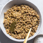 A bowl of cooked lentils with a bay leaf on top.