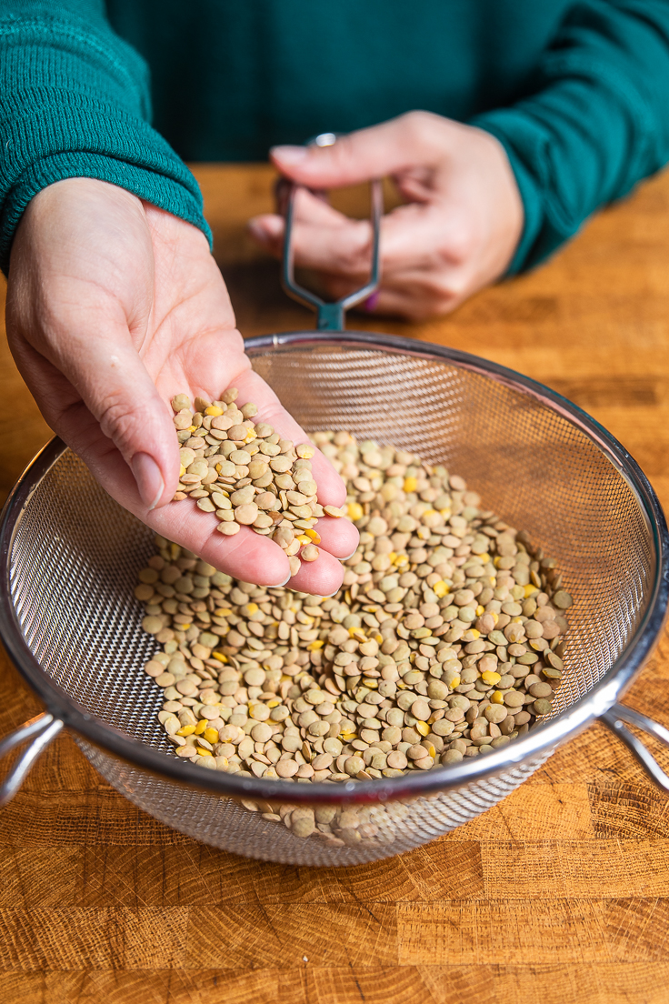 a hand holding dry lentils over a colendar.