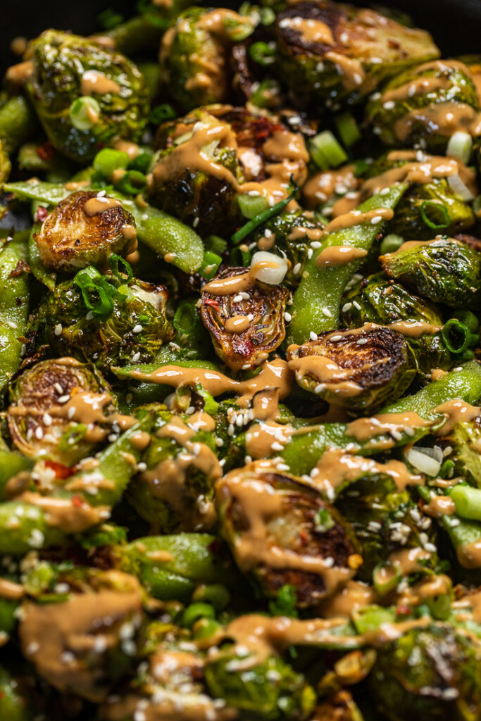 A close up of a pan filled with Brussels sprouts, edamame, and spicy peanut sauce.