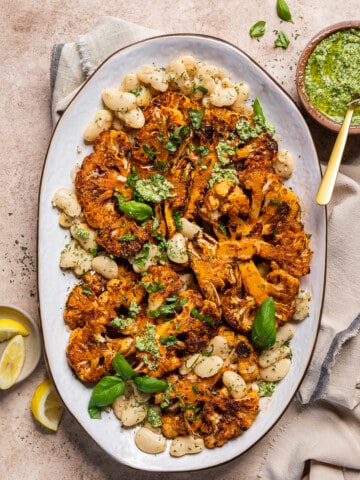 oven roasted cauliflower steaks on a platter with butter beans, pesto and fresh basil.