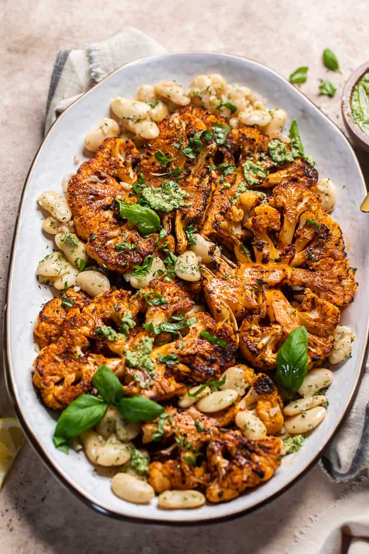 oven roasted cauliflower steaks on a platter with butter beans, pesto and fresh basil. 