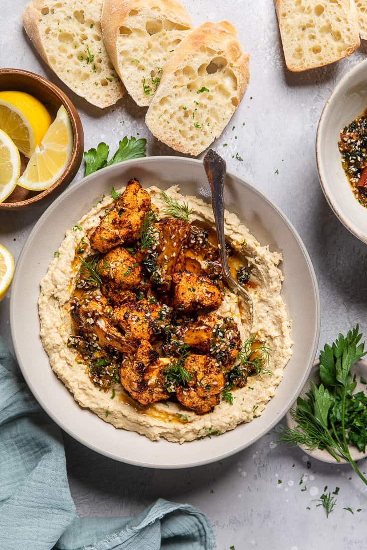bowl of oven roasted cauliflower and hummus with fresh herbs.
