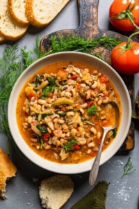 bowl of vegan black eyed peas stew on a table with sliced bread, dill and tomatoes.