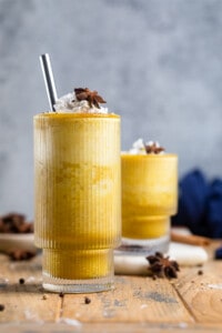 two vegan banana turmeric smoothies in clear classes on a wooden board.