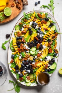 vegan arugula salad on a platter with berries, corn, and grilled mango slices.