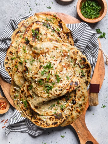 vegan paratha on a wooden cutting board topped with fresh herbs.