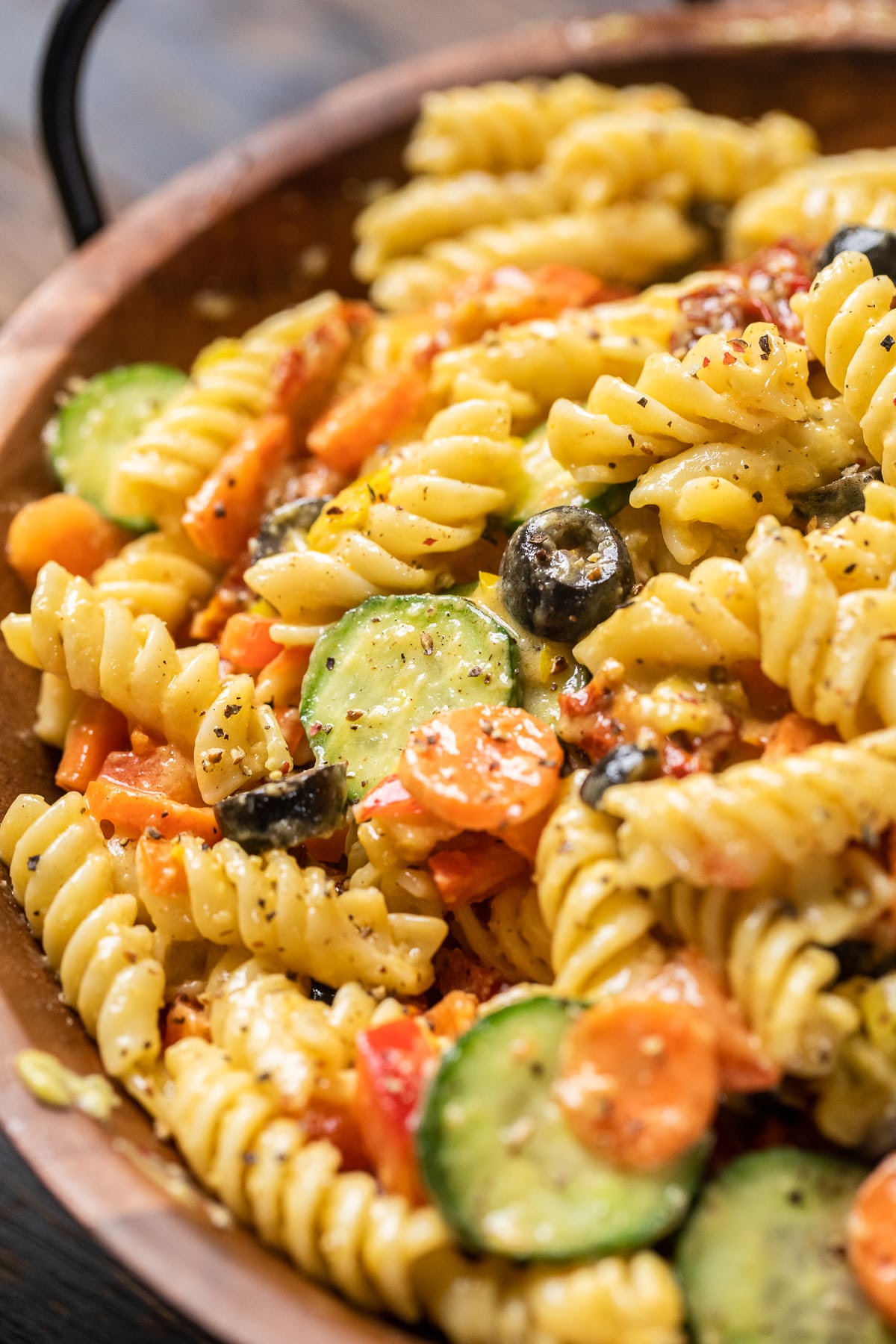 Cremiger veganer italienischer Nudelsalat mit Gurken, Oliven, Karotten und sonnengetrockneten Tomaten.