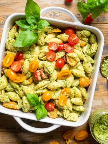 vegan pesto pasta salad in a white square casserole dish with fresh basil.