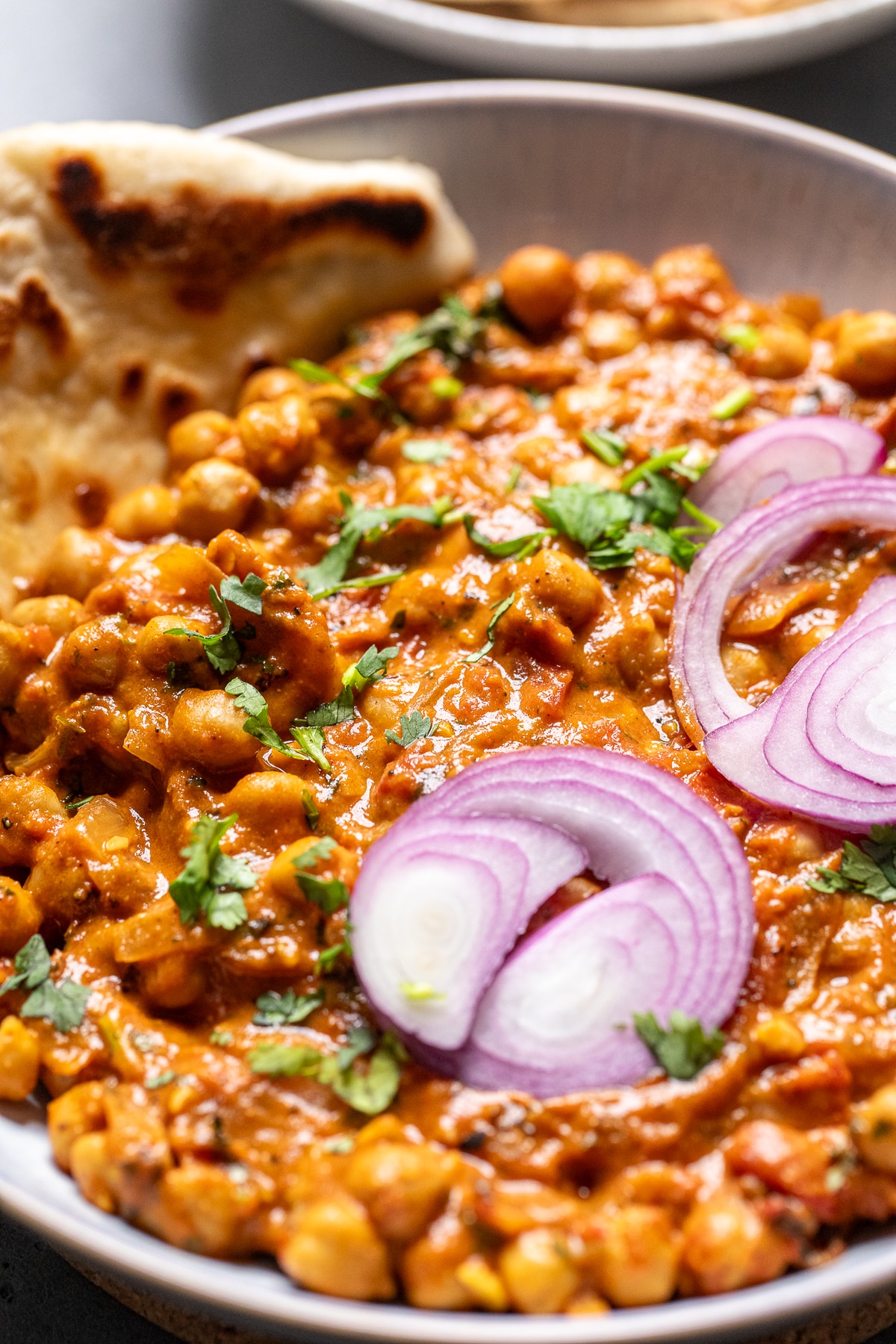 close up of chana masala in a bowl topped with red onions.