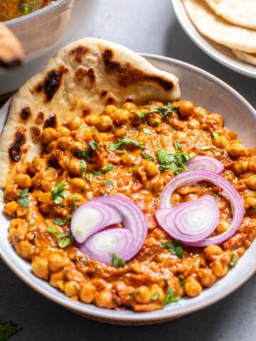 vegan chana masala in a bowl with naan on the side and topped with red onions.