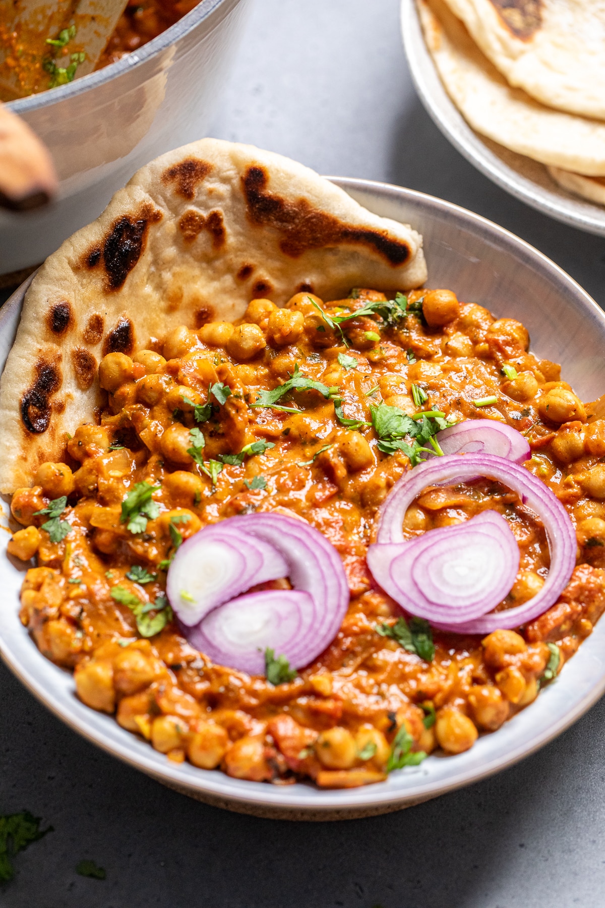 vegan chana masala in a bowl with naan on the side and topped with red onions. 