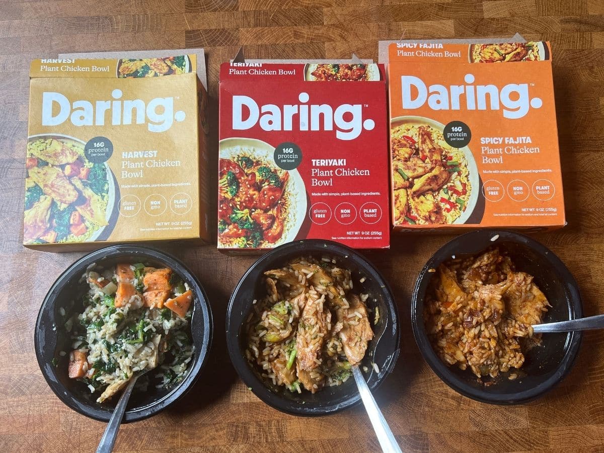 daring foods frozen meals packages and cooked bowls below on a table.