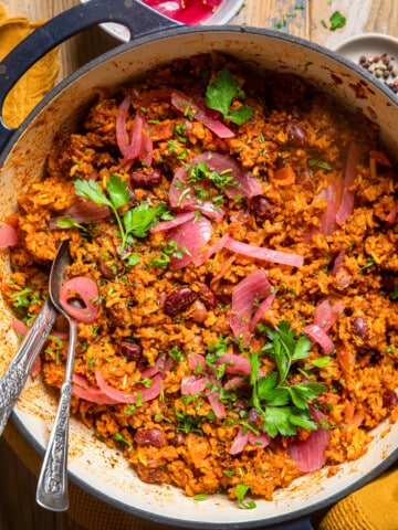 easy vegan jollof rice in a pot topped with pickled onions and cilantro.
