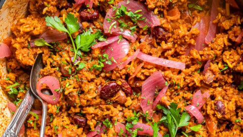 easy vegan jollof rice in a pot topped with pickled onions and cilantro.