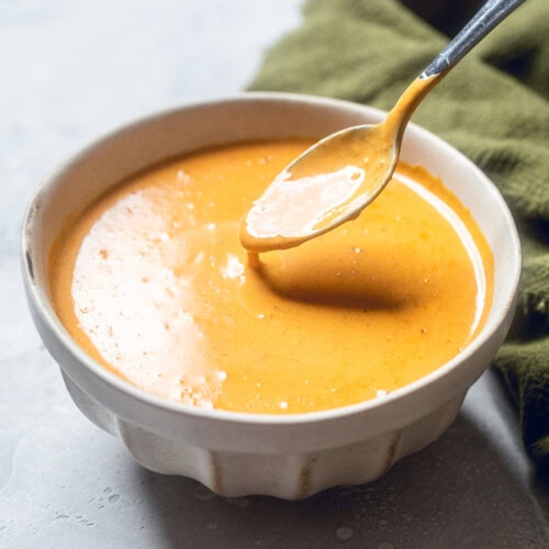 a spoon of red curry sauce dipped in a bowl of sauce.