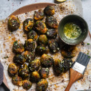 vegan smashed brussels sprouts on a parchment lined plate with a lemon garlic butter sauce.