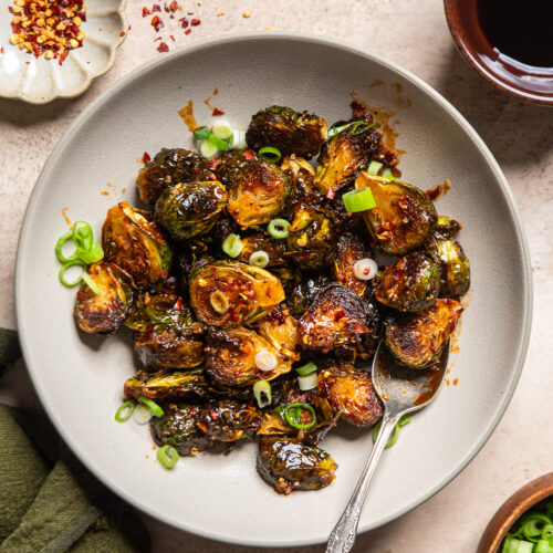 smashed brussels sprouts in a bowl with a maple gochujang sauce over.