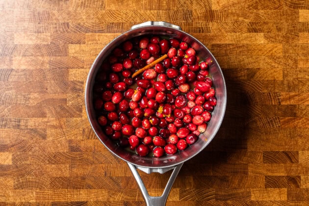 ingredients for cranberry sauce in a stainless steel pot on a table.