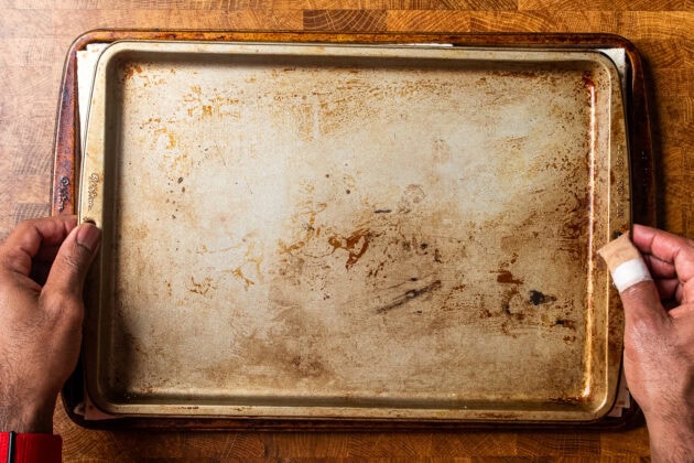 hands placing a baking tray on top of a sheet pan quesadilla prior to cooking.