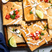 slices of vegan buffalo chicken sheet pan quesadilla topped with lime wedges, diced tomatoes, and vegan sour cream.