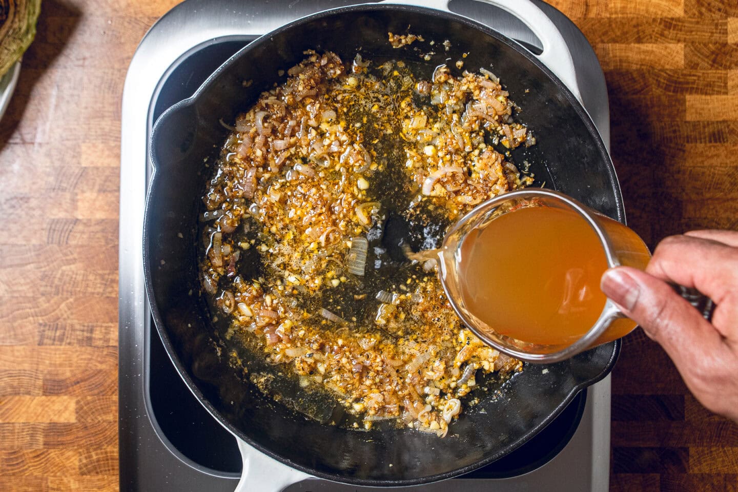 vegetable stock being poured into a skillet of aromatics.