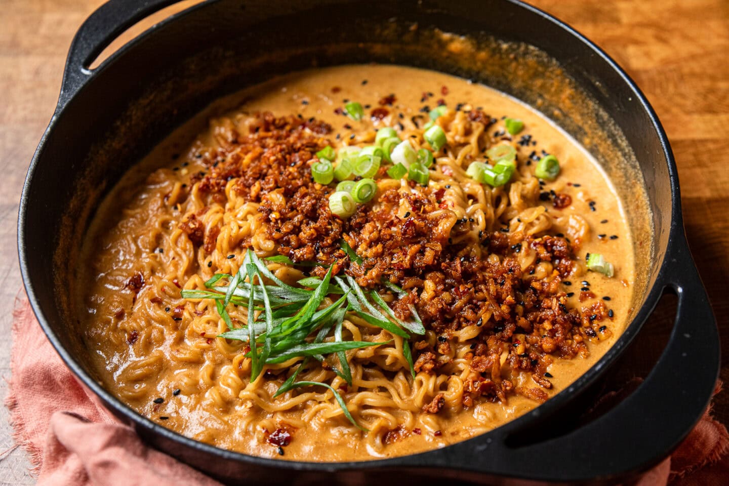 creamy peanut butter ramen in a pot topped with shredded spiced tofu and green onions.