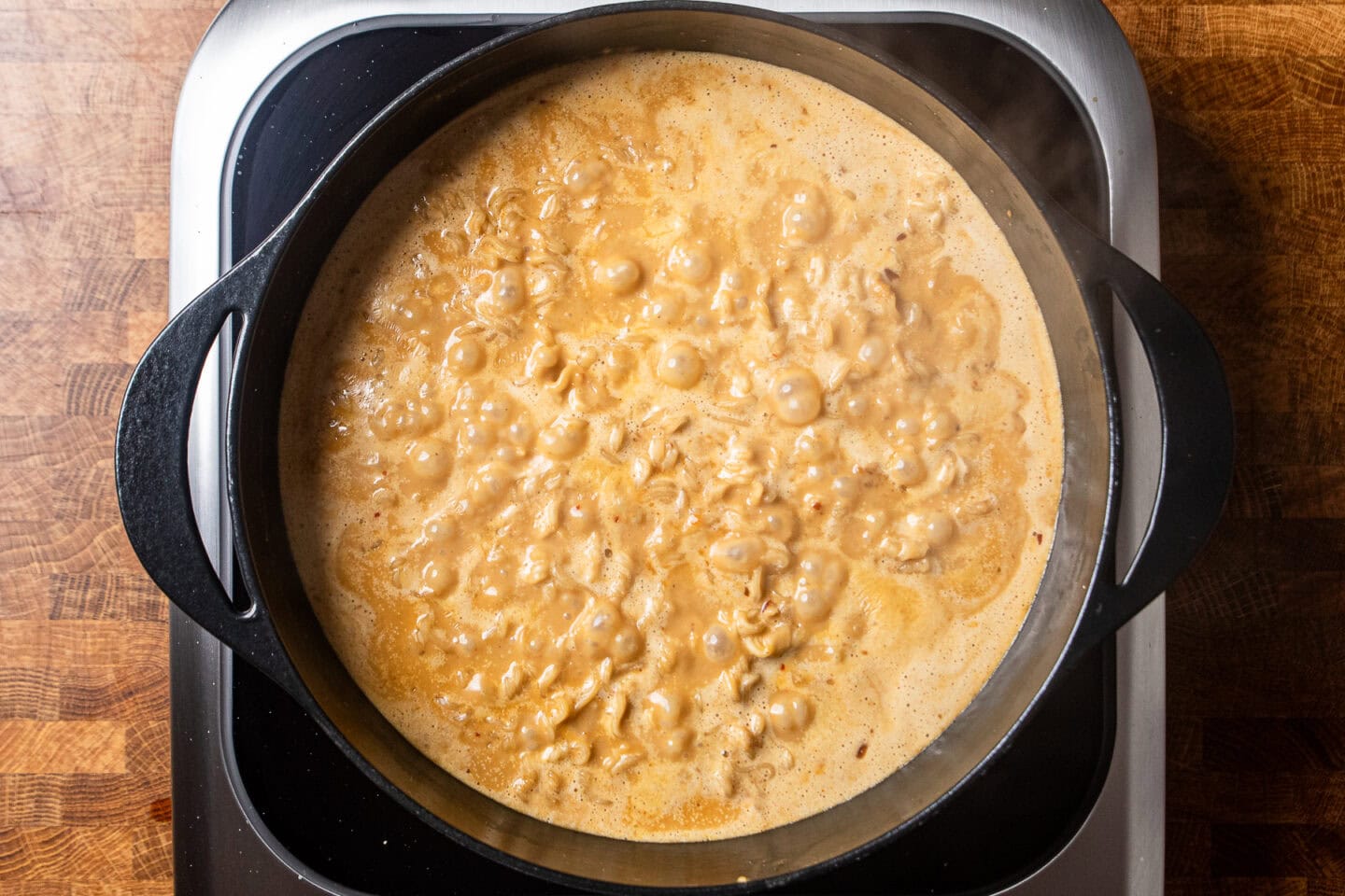 ramen noodles simmering in a pot of peanut butter broth.