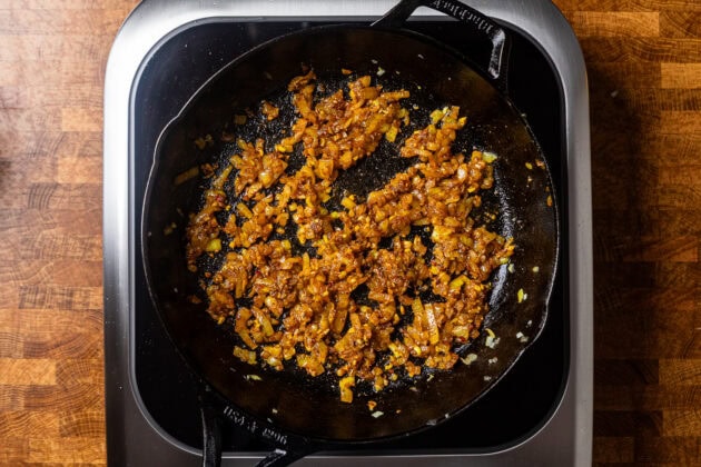 a cast iron skillet of yellow onions sauting mixed with seasonings.
