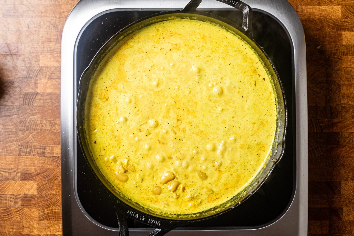 a skillet with a yellow liquid mixture and butter beans inside cooking.