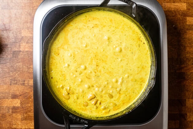 a skillet with a yellow liquid mixture and butter beans inside cooking.