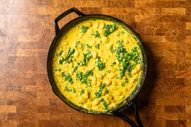 zesty butter beans with kale cooked in a cast iron skillet sitting on a wooden table.