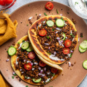 two pitas with mediterranean spiced baked tofu crumbles topped with sliced cucumbers and tomatoes and chopped red onions.