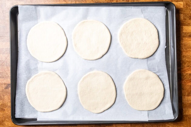 uncooked pitas on a parchment lined baking tray.