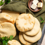a bunch of homemade pitas sitting on a table next to a green napkin and a small wooden bowl filled with butter pats.